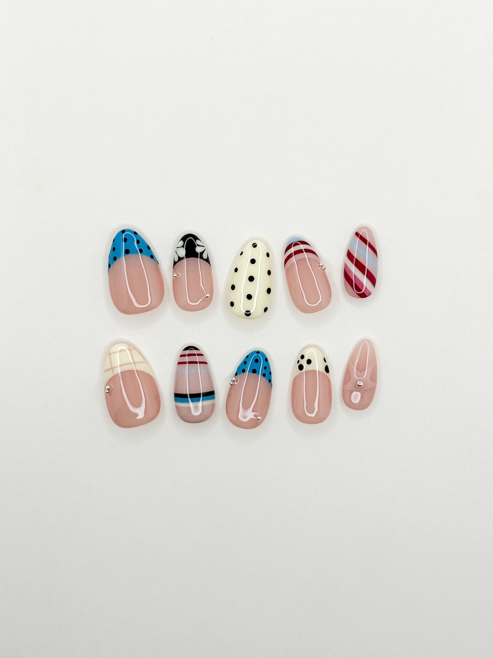 Stripe Club handmade reusable press-on nails laid flat, featuring striped nail art, polka dot French tips, soft nude bases and glossy short almond shapes.
