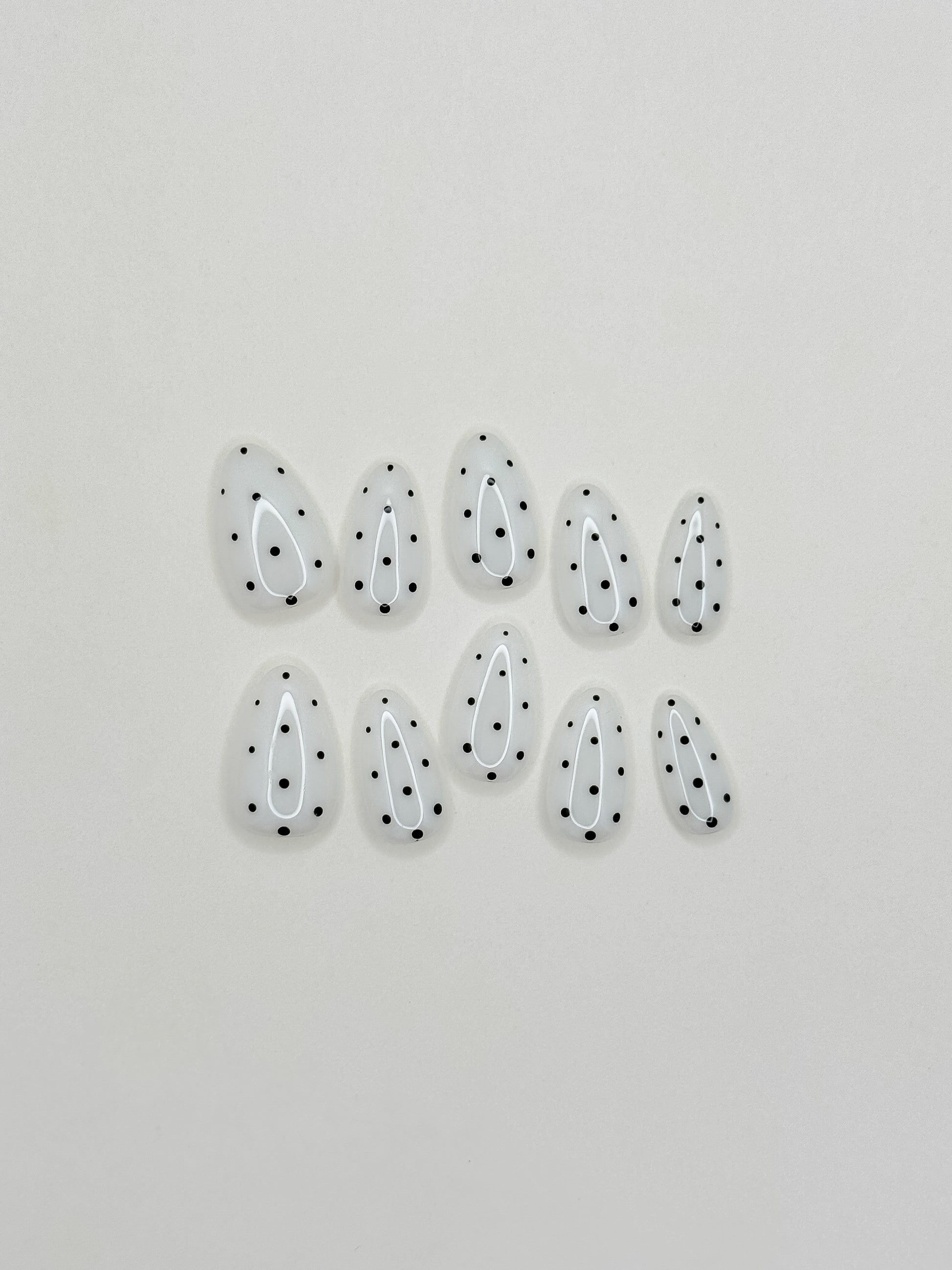 Cream white press-on nails with black polka dot nail art in a glossy short almond shape. Handmade reusable false nails inspired by retro mod fashion, monochrome minimalist nails and vintage polka dot manicure styles.