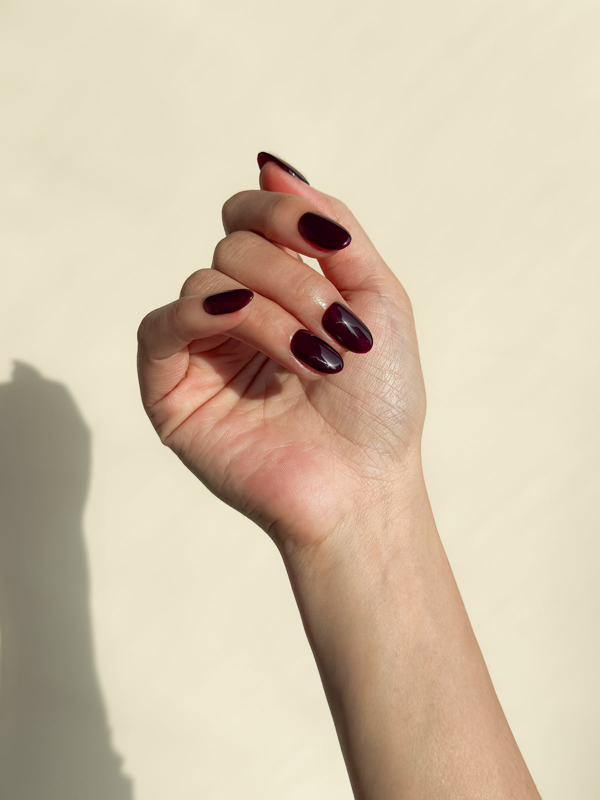 Close-up of a hand wearing After Work dark cherry burgundy short oval press-on nails with a high-gloss finish.