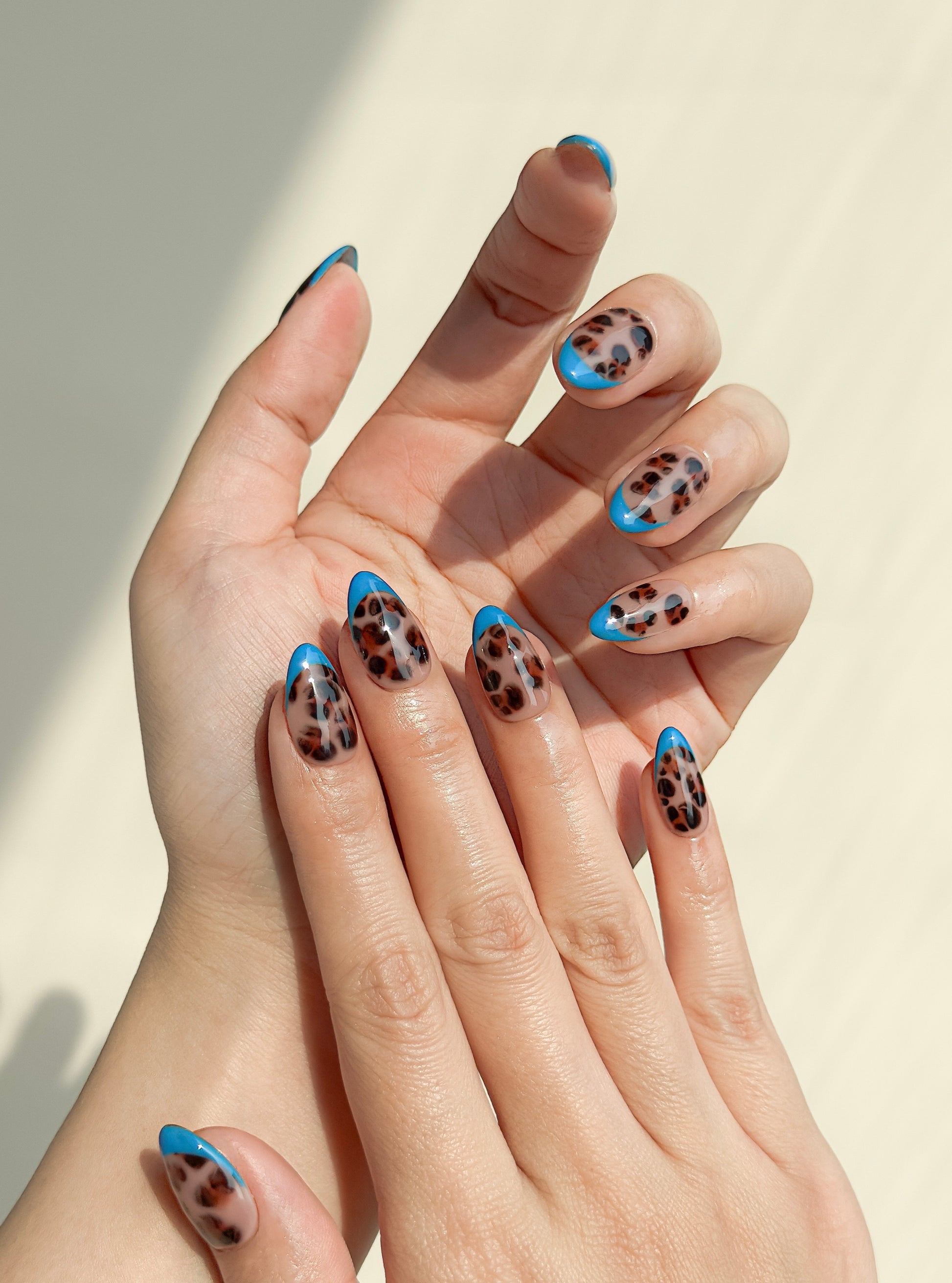 Blue Monday handmade short almond press-on nails worn on two hands, featuring glossy tortoiseshell nail art with bold cobalt blue French tips.