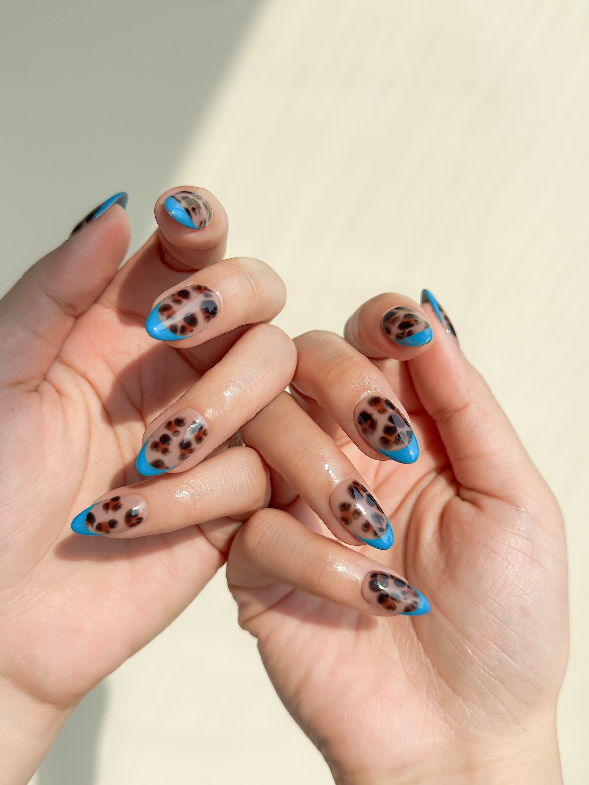 Blue Monday handmade short almond press-on nails worn on two hands, featuring glossy tortoiseshell nail art with bold cobalt blue French tips.