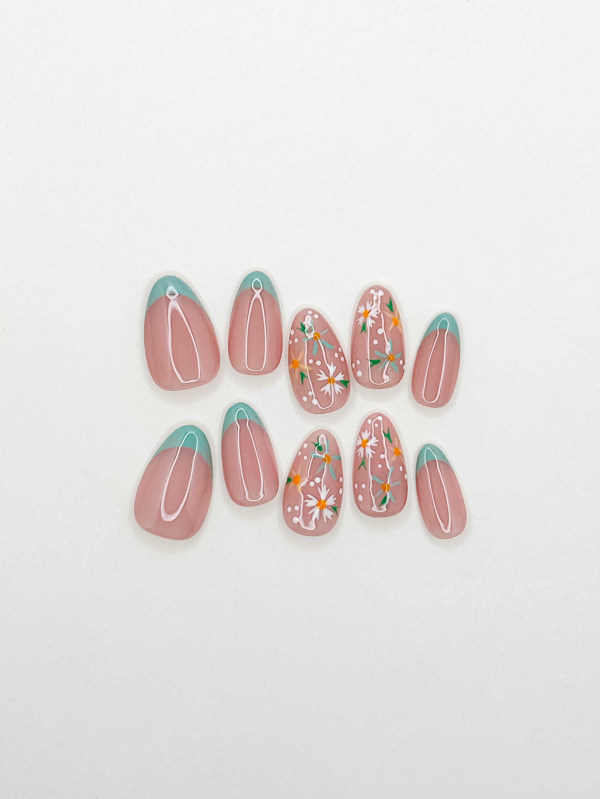 Daisy Chain handmade press-on nails arranged on a white background, featuring short almond nails with mint skinny French tips, white daisies, orange flower centres and dotted details.
