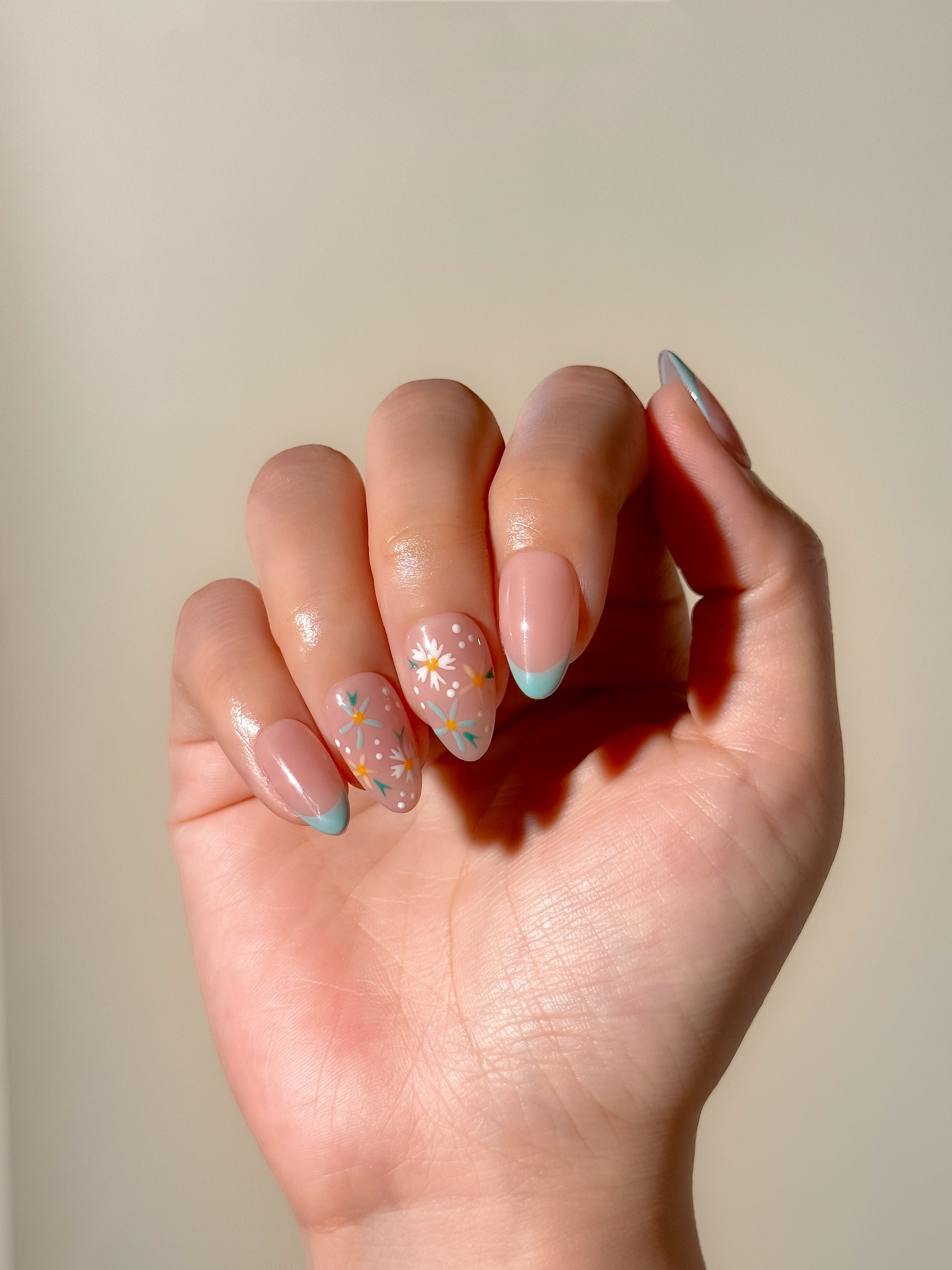Daisy Chain short almond press-on nails worn on hand, featuring soft mint French tips and hand-painted white daisy nail art over a sheer blush base.