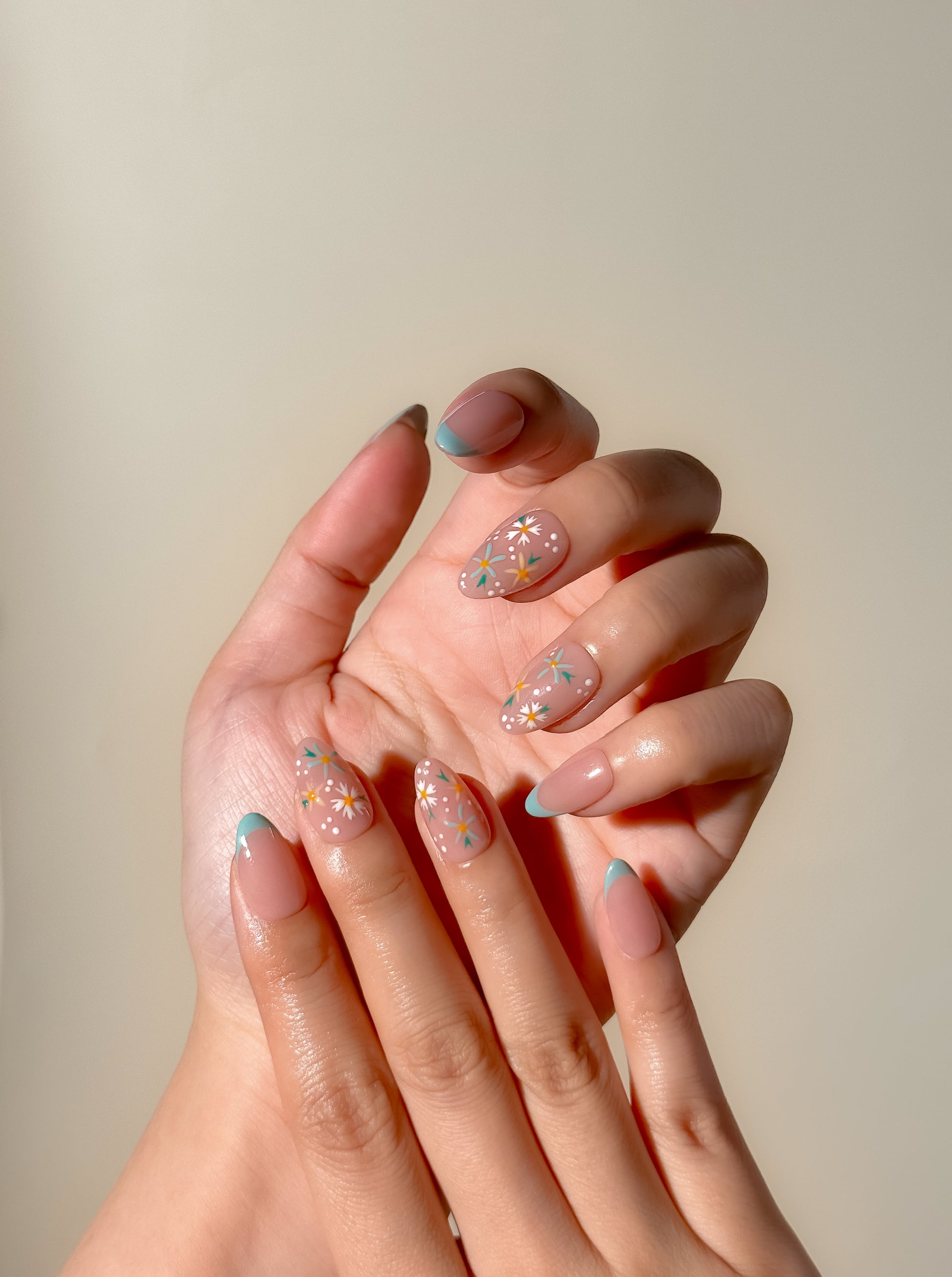 Daisy Chain handmade press-on nails worn on two hands, featuring short almond mint French tips, white floral accent nails and delicate dotted details.
