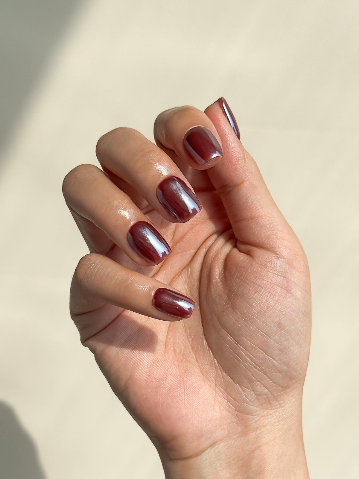 Close-up of a hand wearing Deadline glazed brick-red short square press-on nails with a luminous high-shine finish.