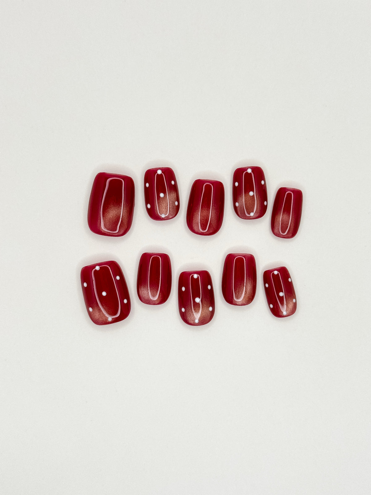 Expense Account dark red cat-eye short square press-on nails with white polka dots arranged on a white background.