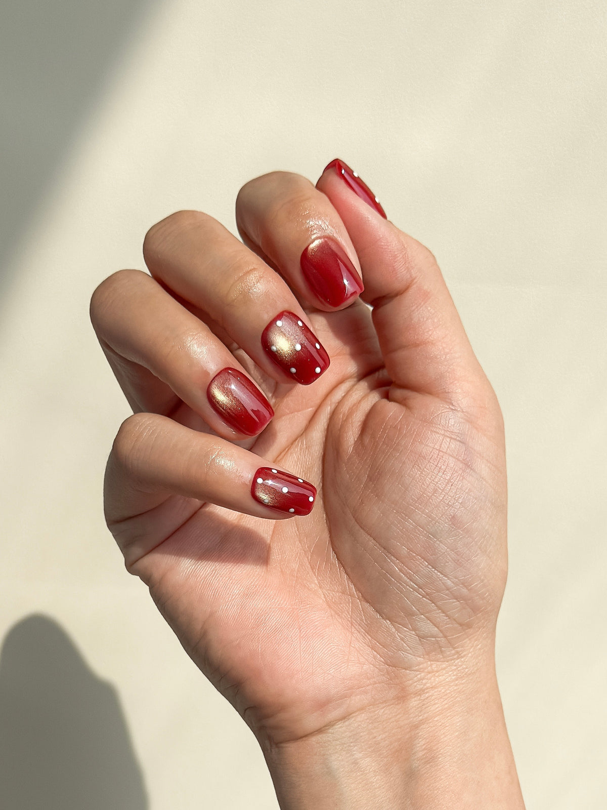 Expense Account dark red cat-eye short square press-on nails with white polka dots arranged on a white background.