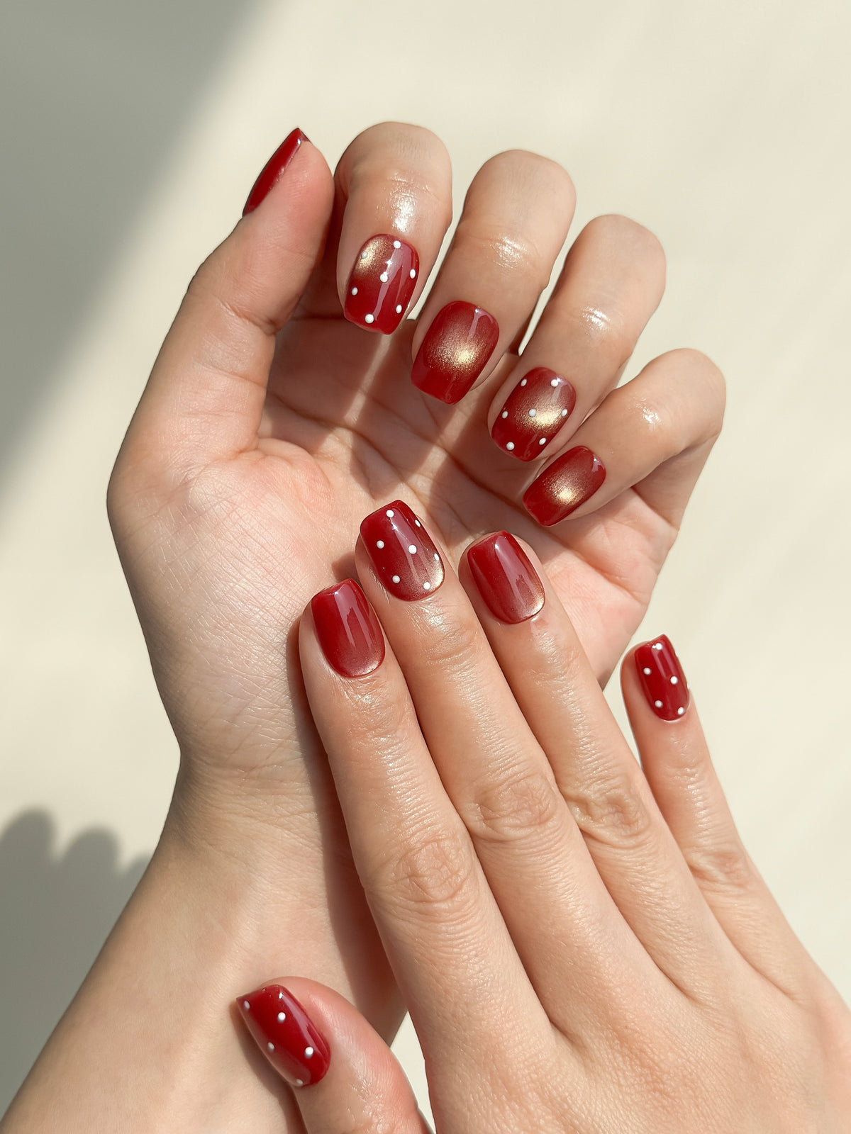 Two hands wearing Expense Account dark wine-red cat-eye and polka-dot short square press-on nails.