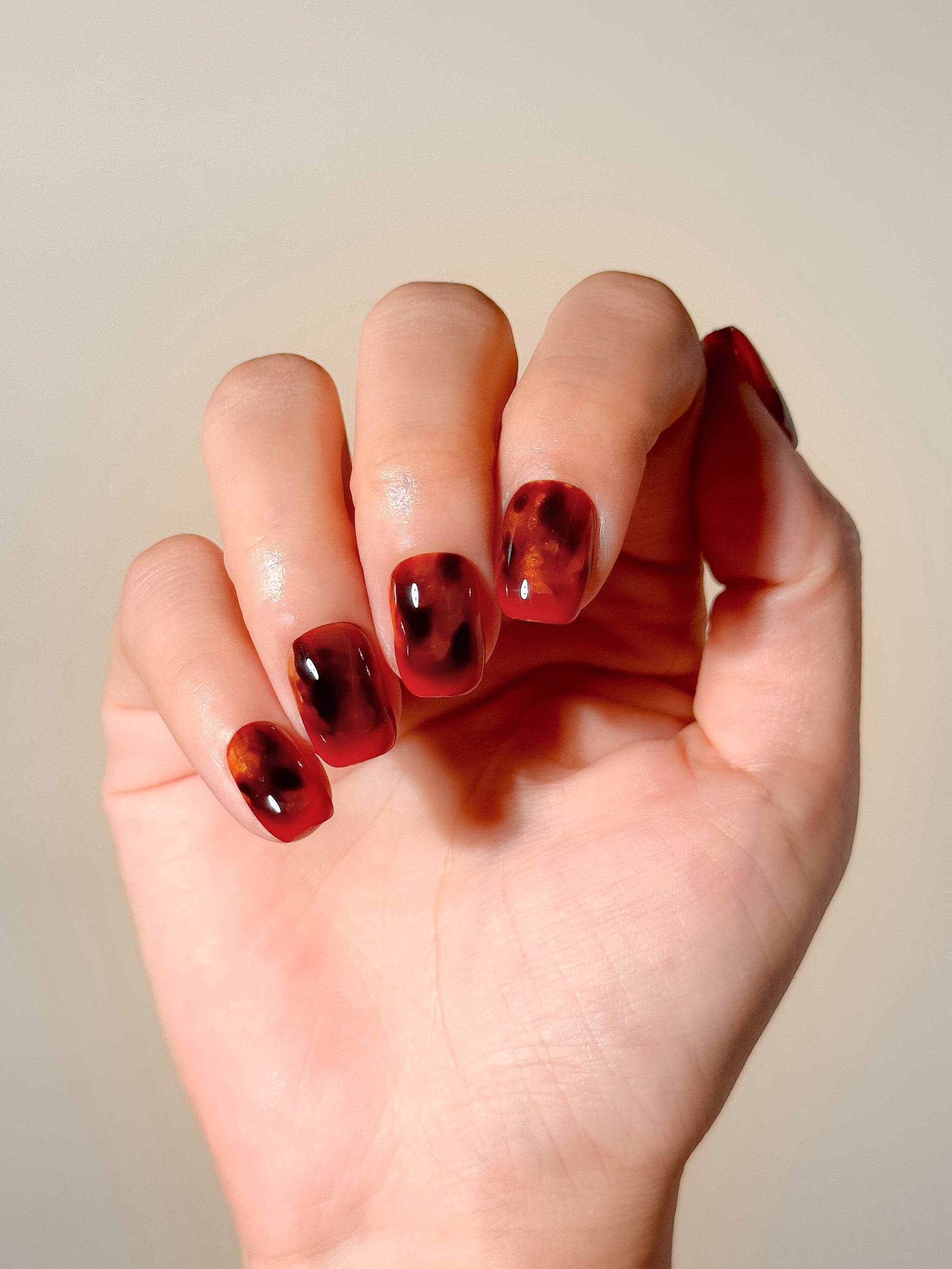 Heat Wave handmade short square press-on nails worn on hand, featuring a glossy translucent red base with amber and dark tortoiseshell-inspired detailing.