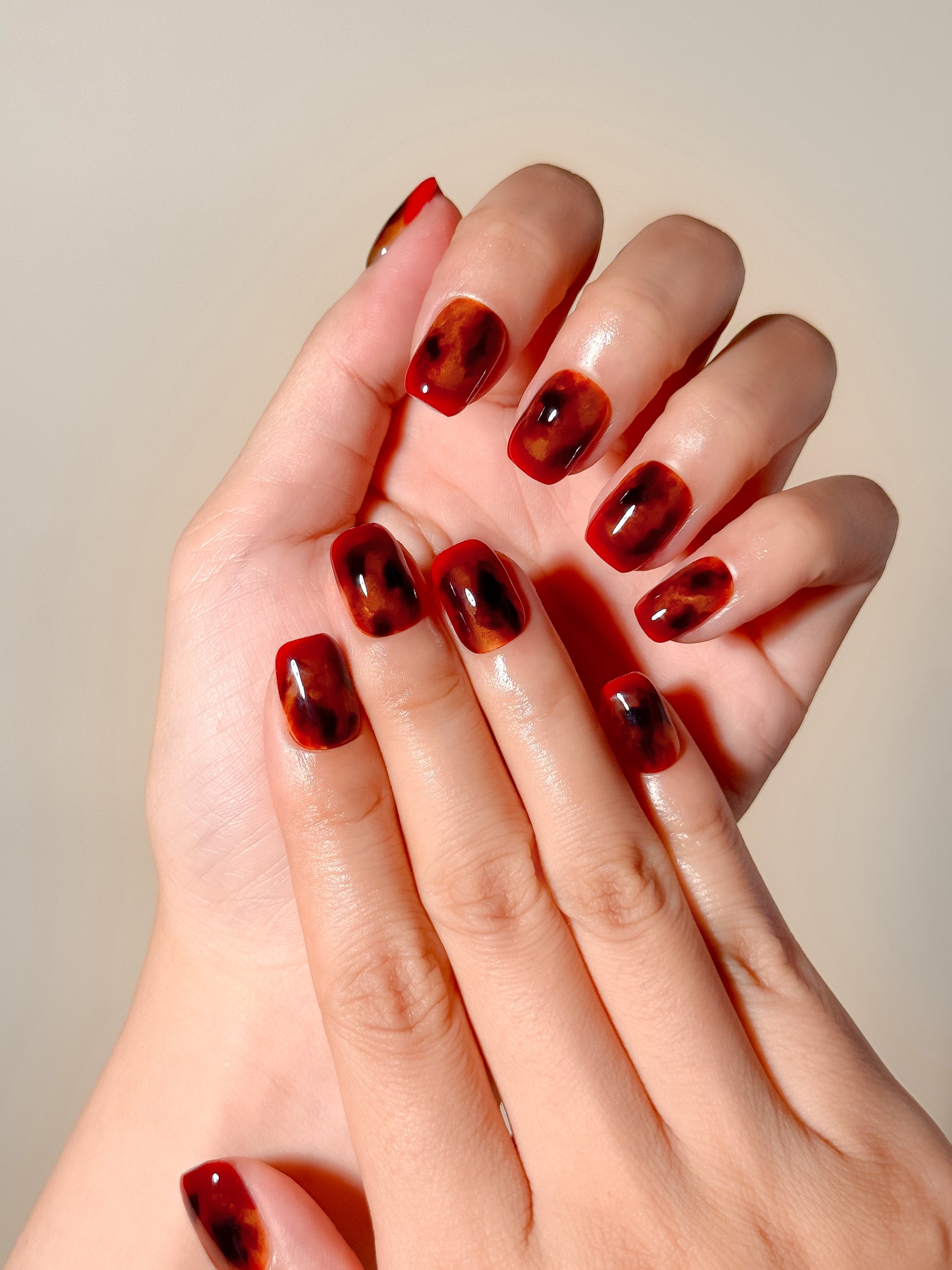Heat Wave handmade short square press-on nails worn on hand, featuring a glossy translucent red base with amber and dark tortoiseshell-inspired detailing.