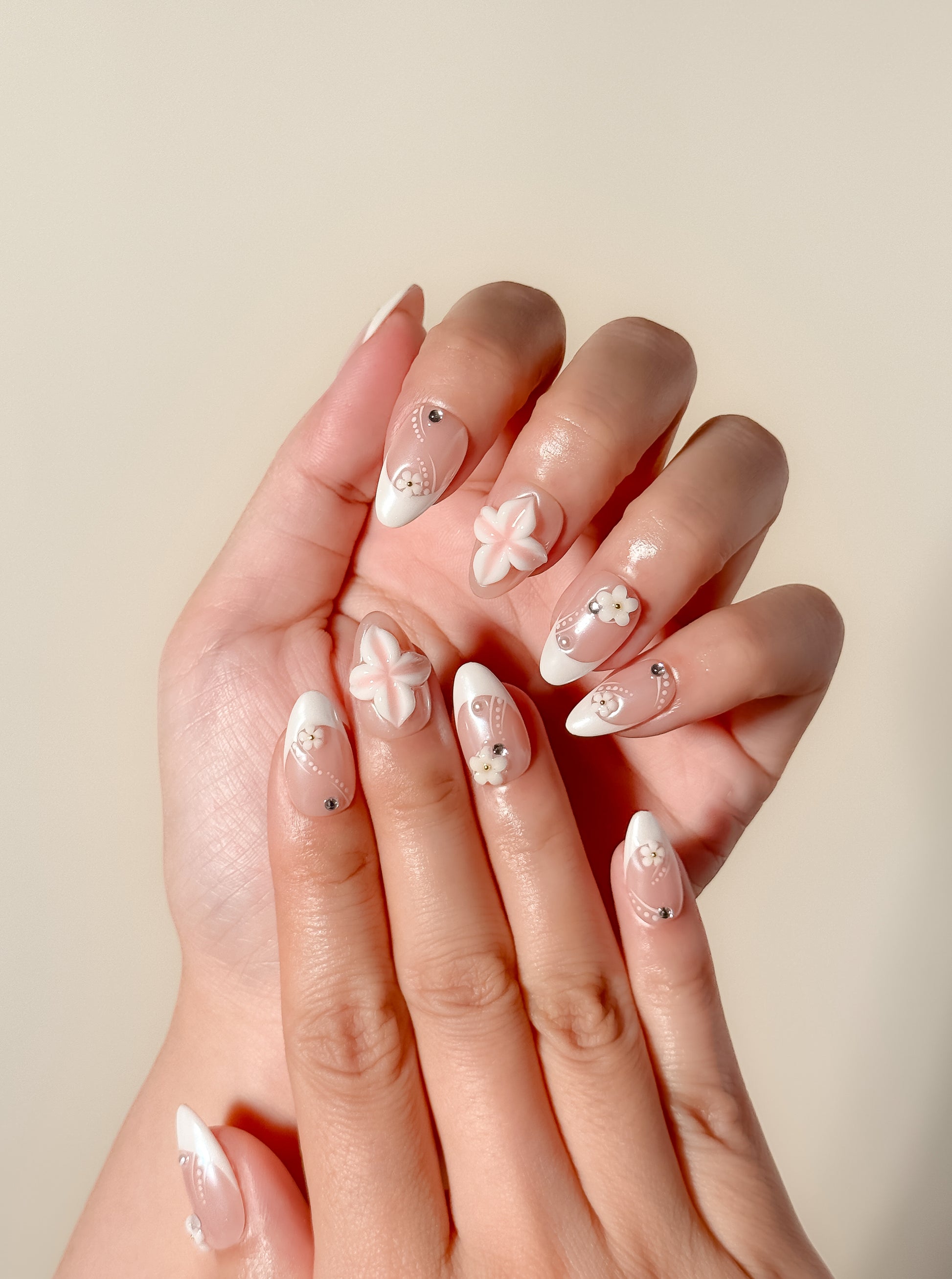 Last Call handmade short almond nails worn on two hands, with blush bases, white French tips, 3D floral accents and silver studs.