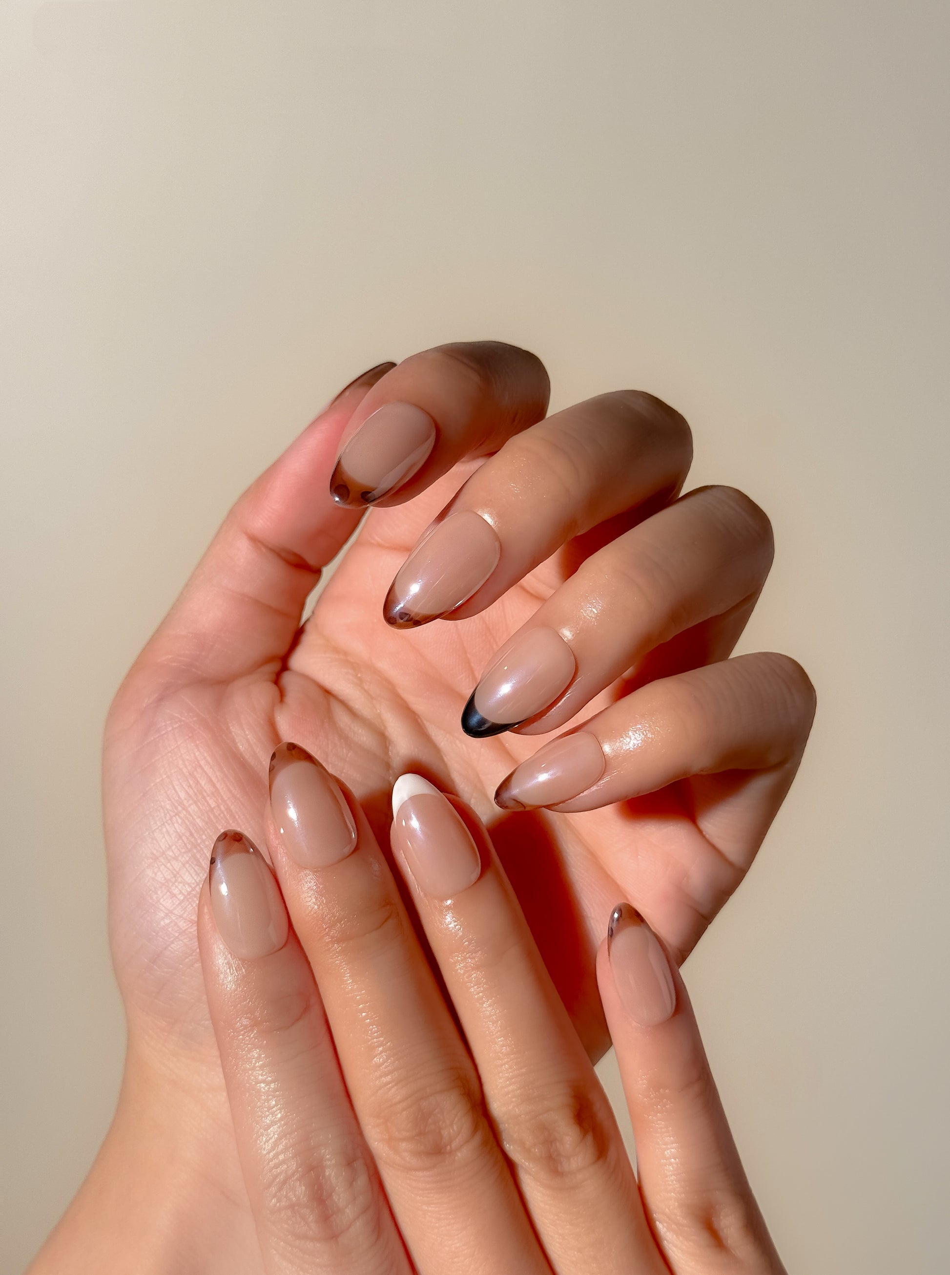 Mixed Signals short almond press-on nails worn on two hands, featuring ultra-fine tortoiseshell, black and white French tips with a soft glazed finish.