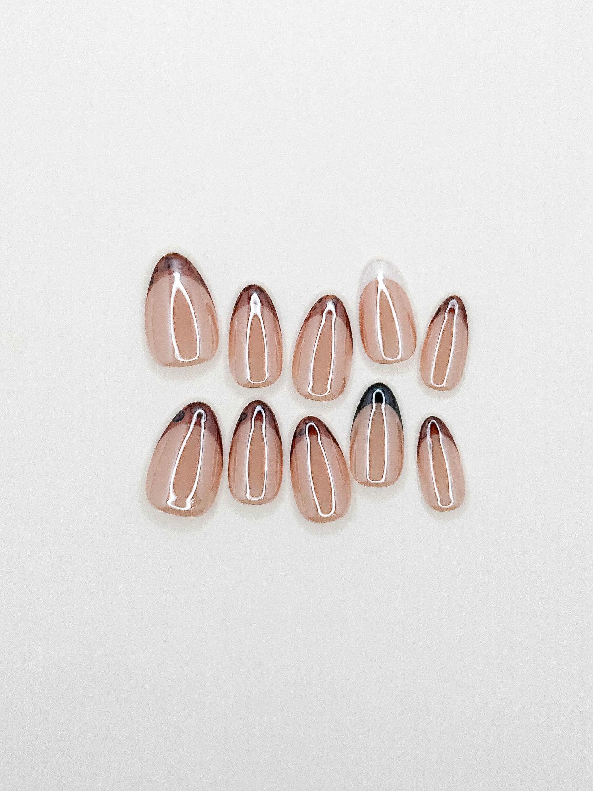 Mixed Signals handmade press-on nails arranged on a white background, featuring glazed short almond nails with tortoiseshell, black and white skinny French tips over a sheer nude base.