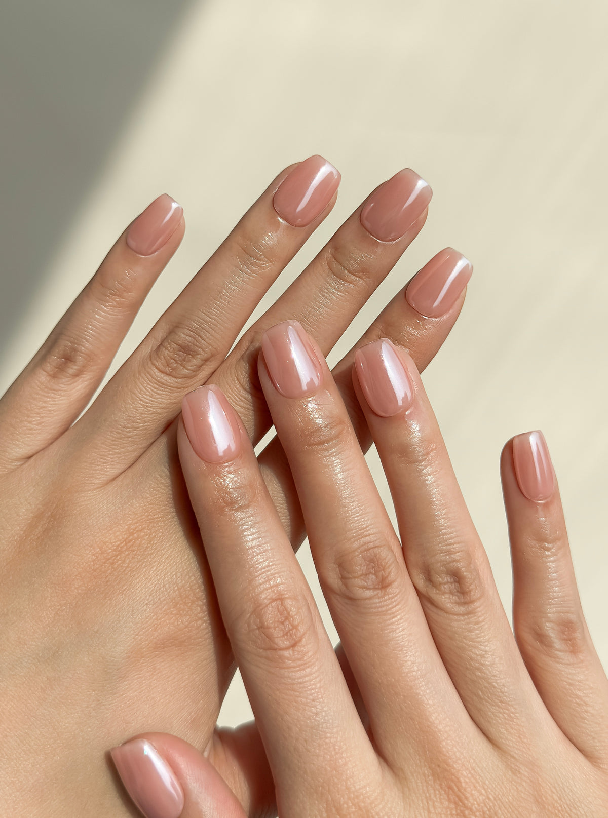 Two hands wearing Morning Commute soft peach glazed short square press-on nails in warm natural sunlight.