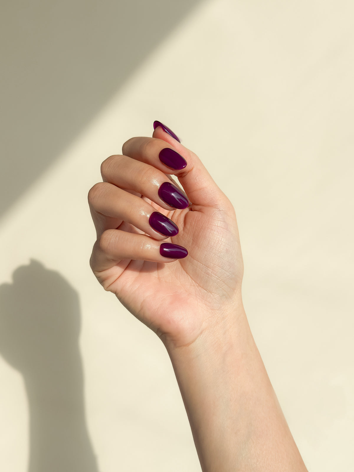 Close-up of a hand wearing Office Crush deep aubergine purple short oval press-on nails with a high-gloss finish.