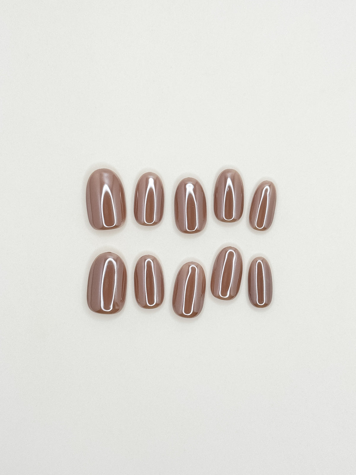 Payday taupe beige nude glazed short oval press-on nails arranged as a luminous reusable set on a white background.