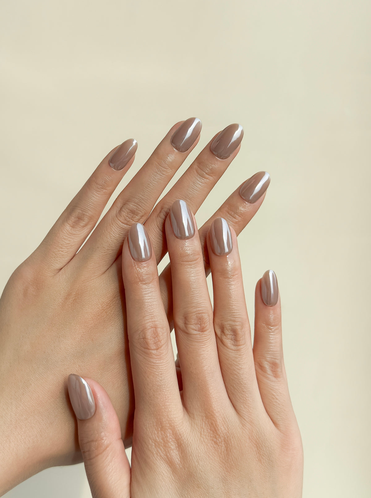 Close-up of a hand wearing Payday taupe nude short oval press-on nails with a luminous glazed chrome finish.