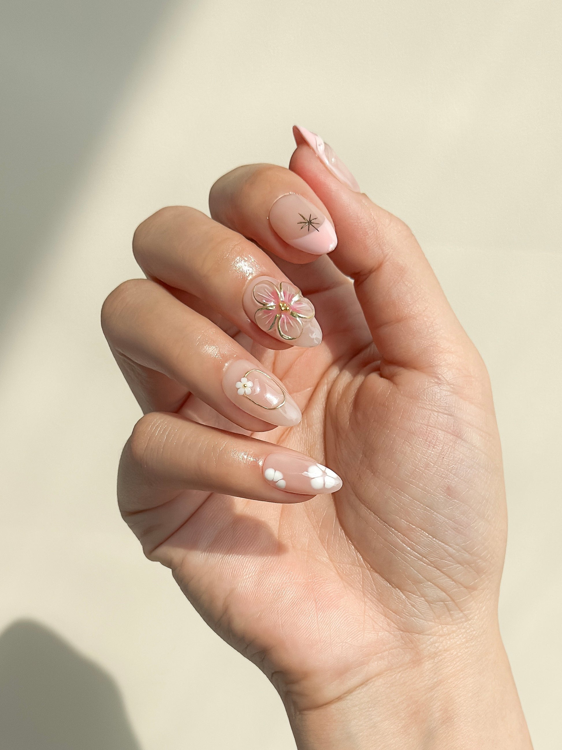 Petal handmade pink 3D flower press-on nails worn on one hand, featuring white blossoms, gold details and a glossy short almond shape.