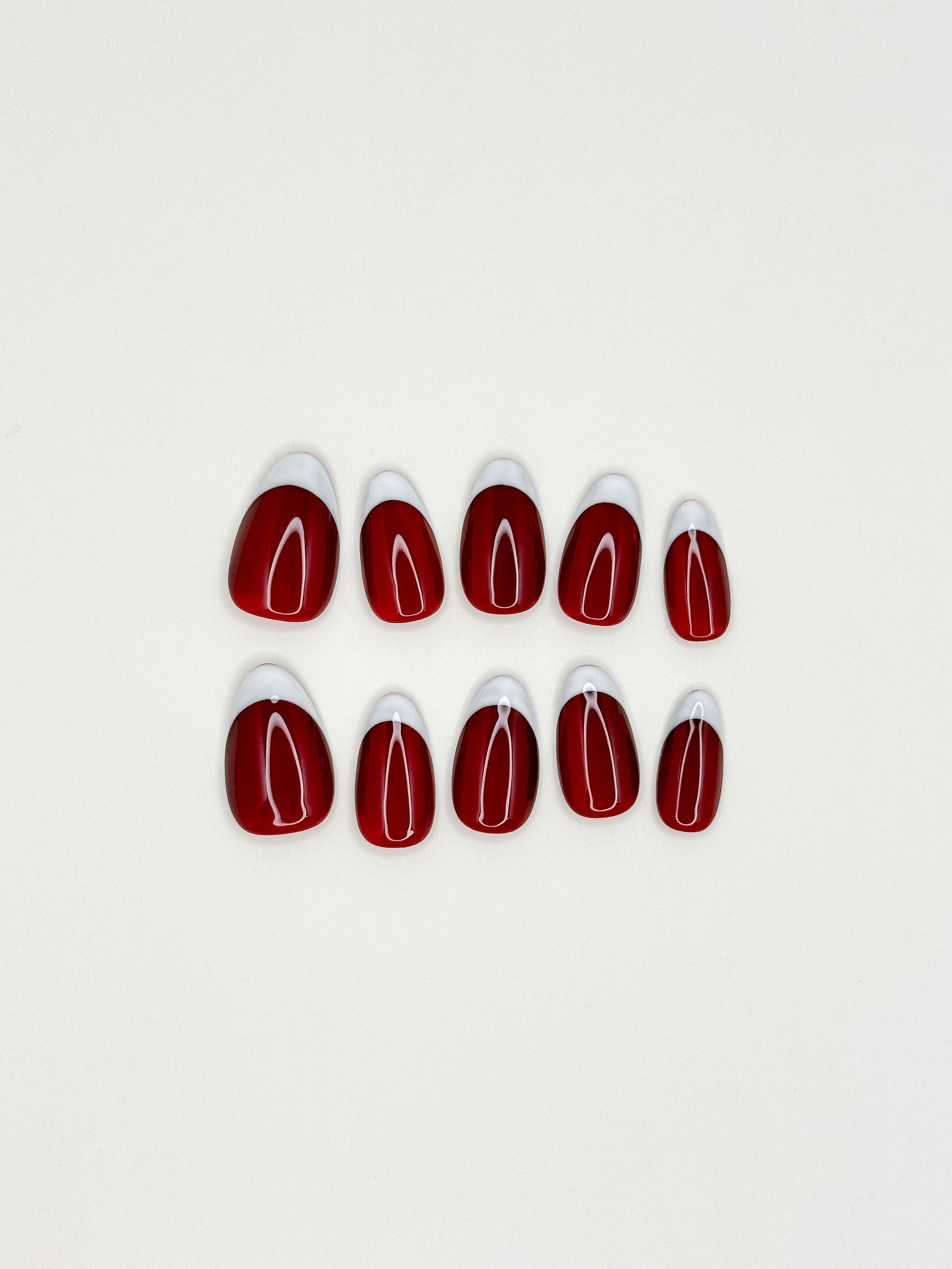 A set of ten false press-on nails arranged in two rows on a plain white background. The nails have a glossy deep red body with a white pointed tip.