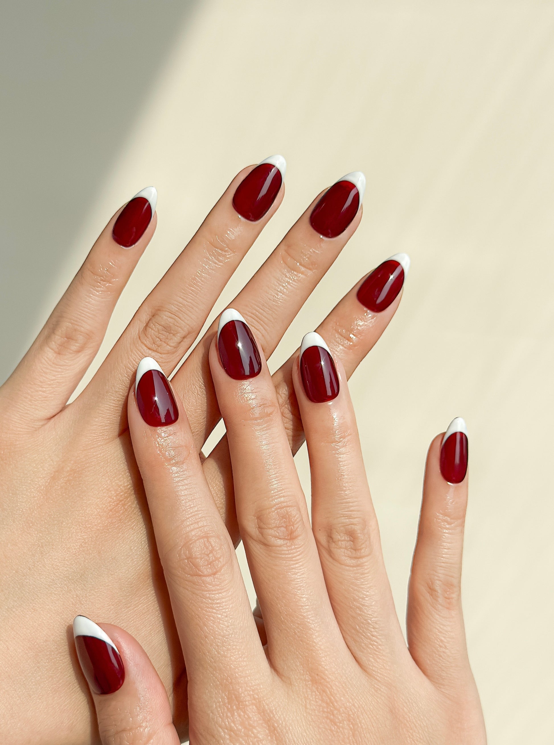 Red Room handmade short almond press-on nails worn on two hands, featuring a glossy deep wine-red base with crisp white French tips.