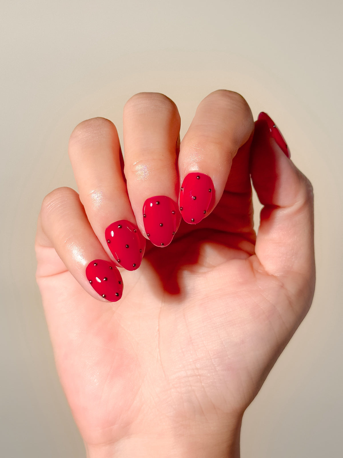 A hand wearing Strike One glossy red extra-short oval press-on nails with silver metallic stud details.
