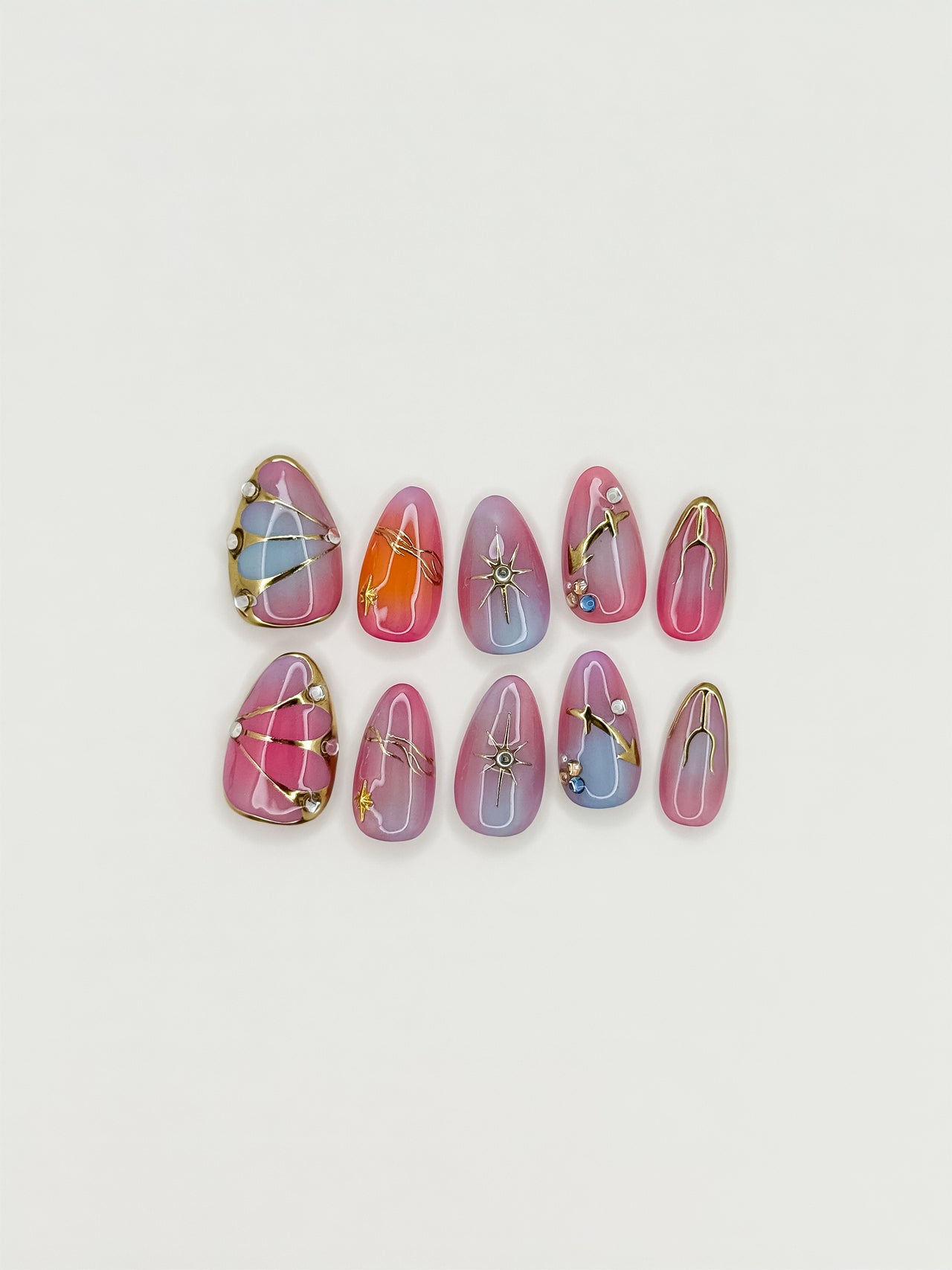 Summer After Dark short almond press-on nails arranged on white, with pink, orange and lilac gradients, metallic celestial lines and crystals.