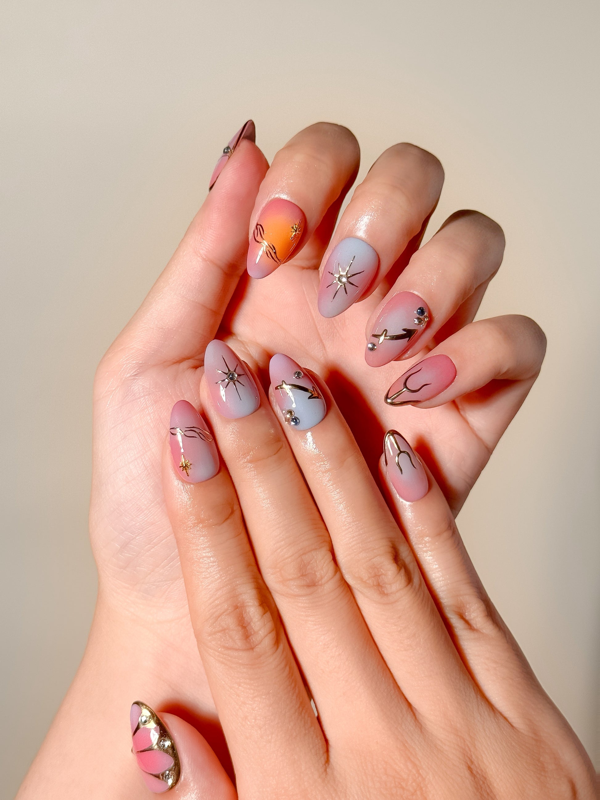 Summer After Dark handmade celestial press-on nails worn on two hands, with pink, coral and lilac aura colours in a short almond shape.
