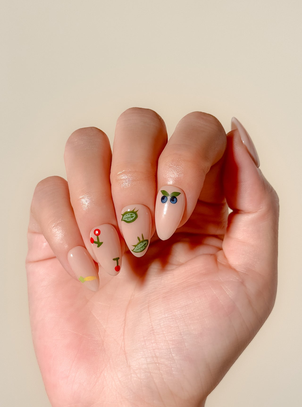 Summer Apron handmade short almond press-on nail set arranged on white, with a glossy nude base and colourful fruit, vegetable, flower and garden-bug illustrations