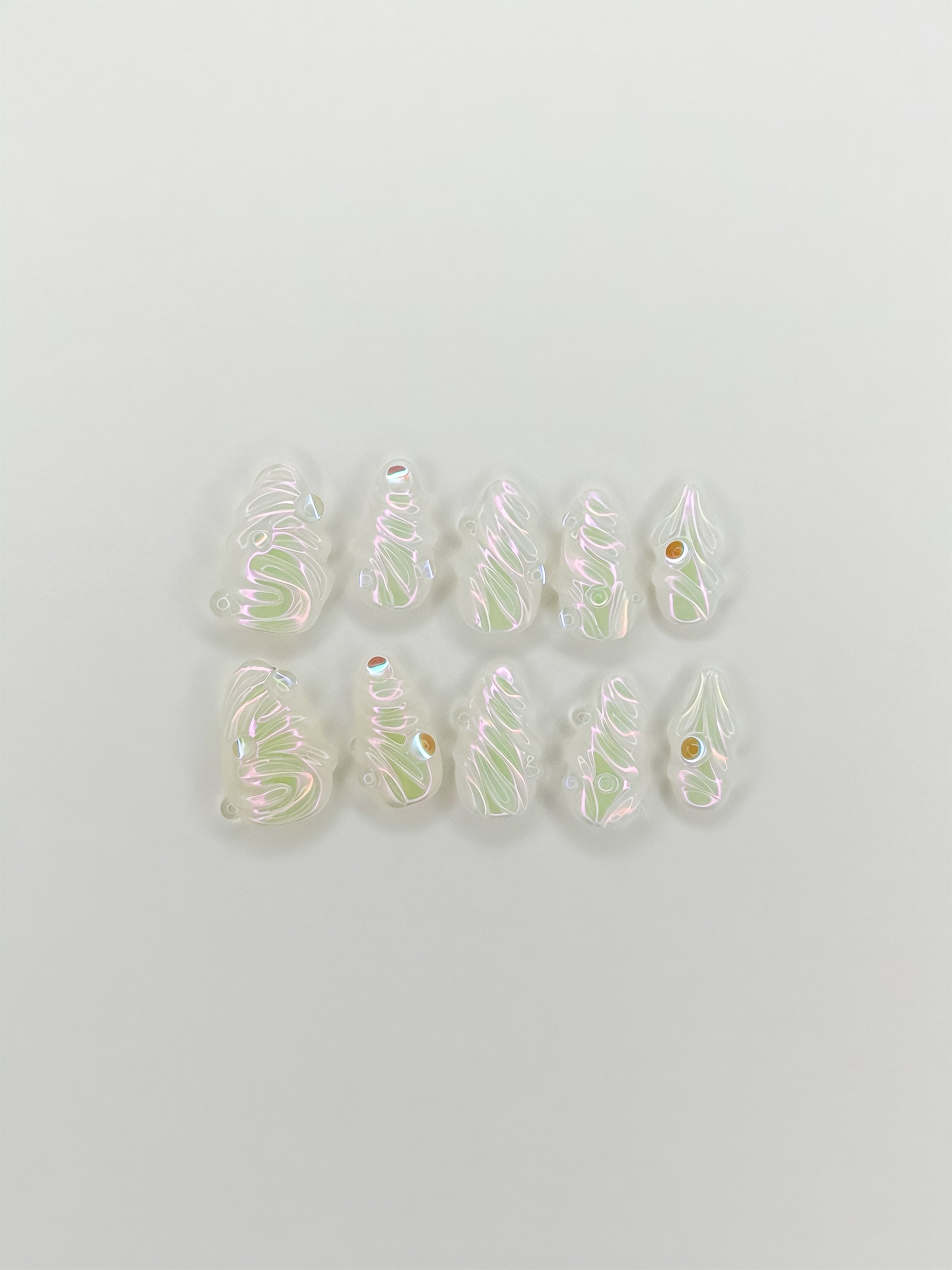 The Encore handmade short almond press-on nails arranged on white, with pearlescent 3D swirls, iridescent shimmer and tiny gold studs.