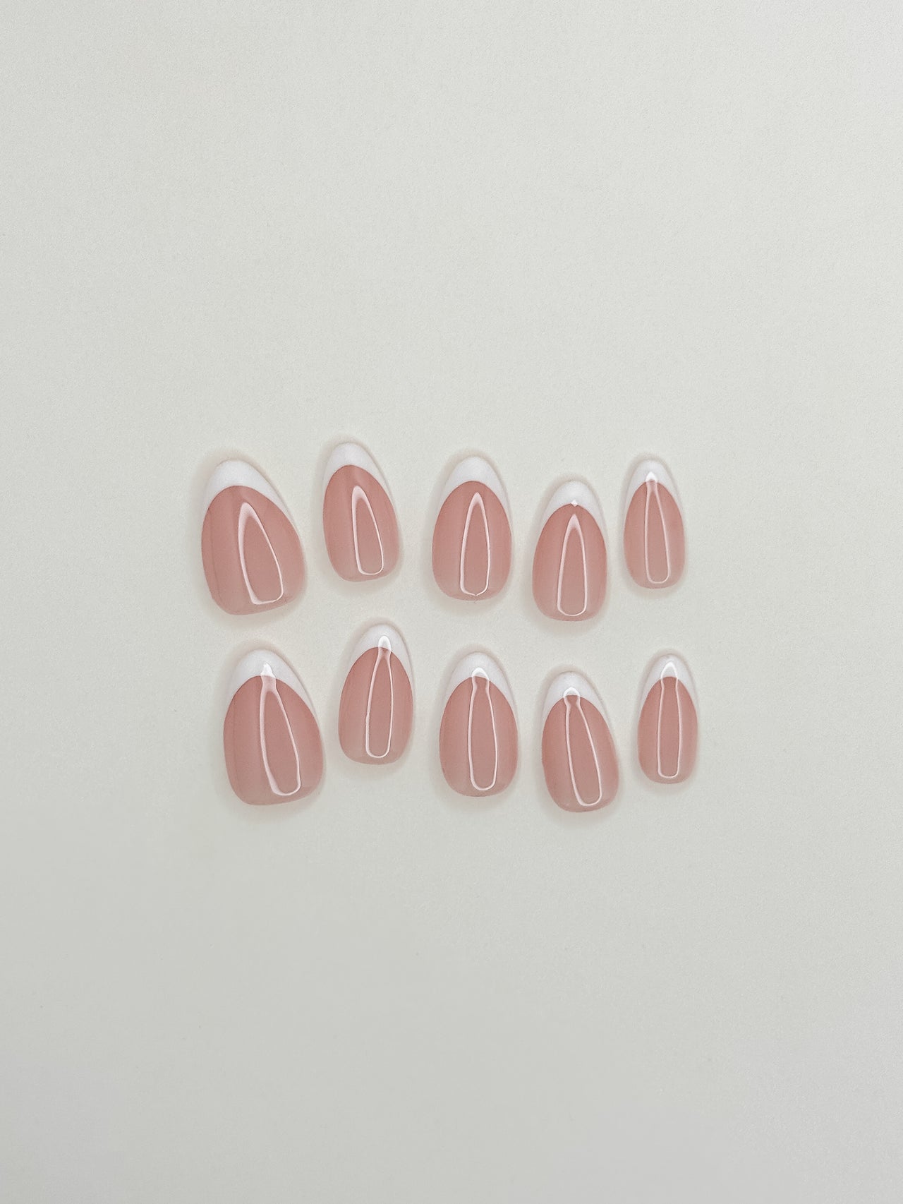 The Original handmade press-on nails arranged on a white background, featuring short almond nails with crisp white skinny French tips over a sheer blush-pink base.