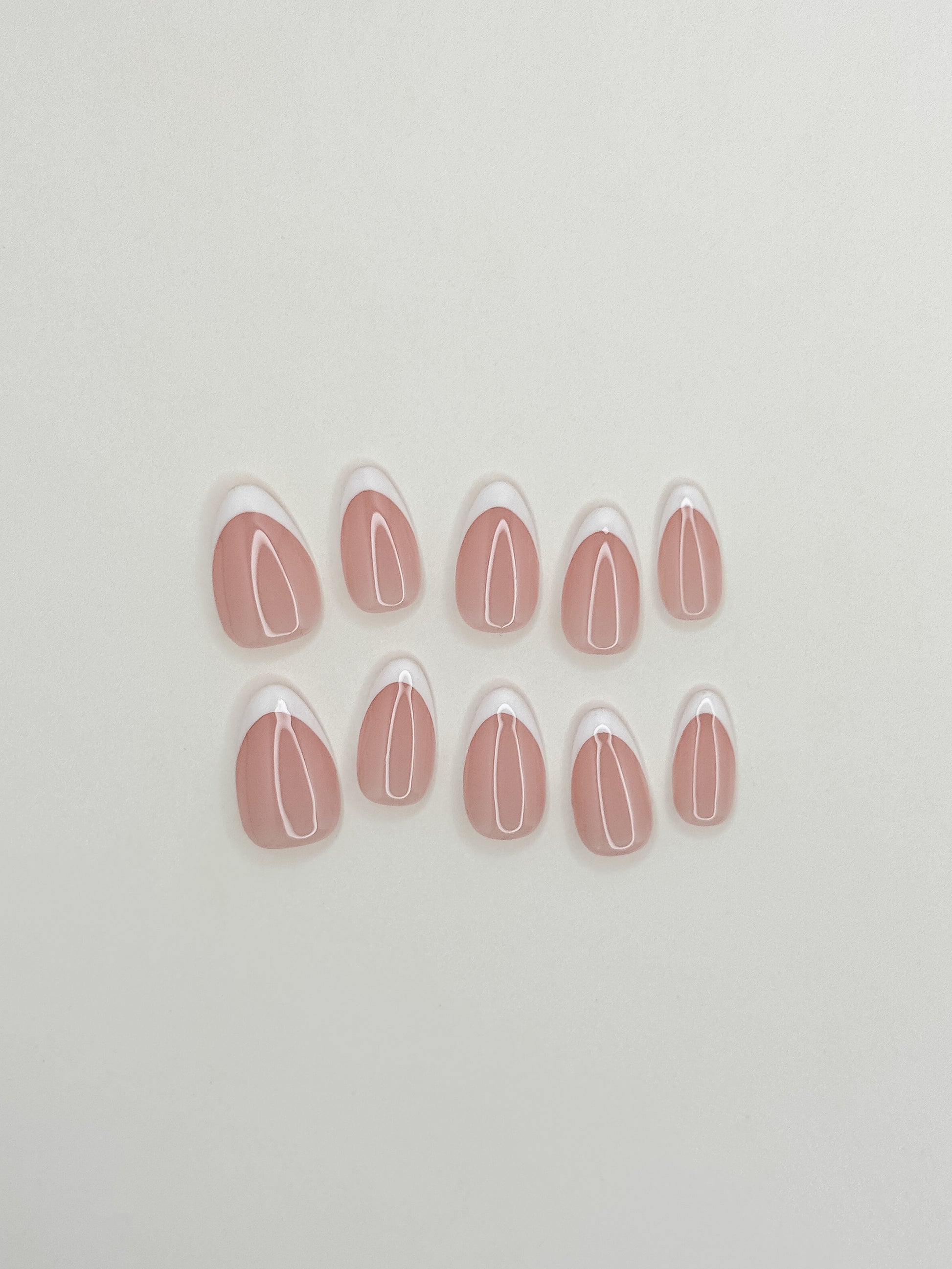 The Original handmade press-on nails arranged on a white background, featuring short almond nails with crisp white skinny French tips over a sheer blush-pink base.