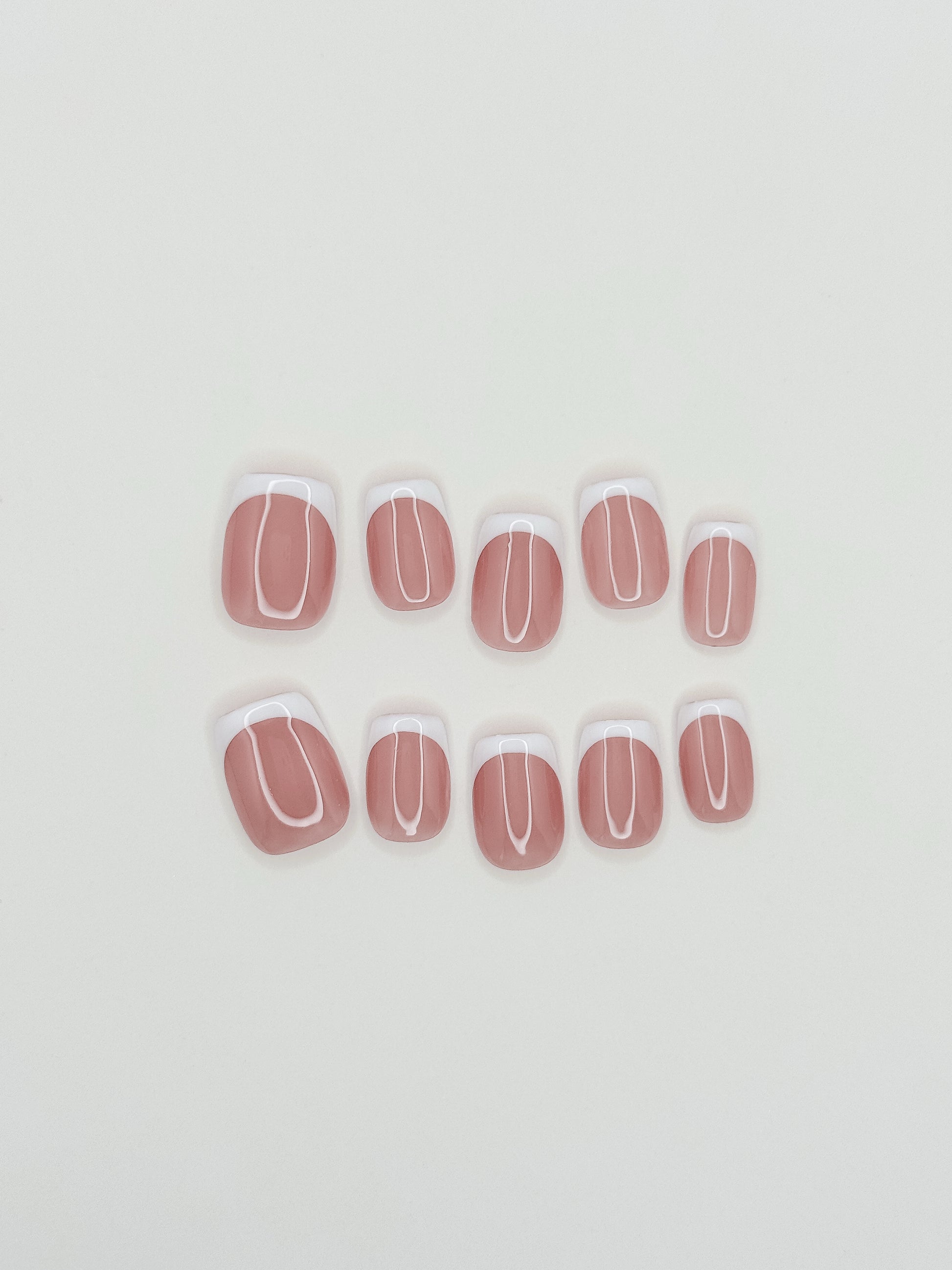 The Short Cut handmade press-on nails arranged on a white background, featuring short square nails with crisp white skinny French tips over a sheer blush-pink base.