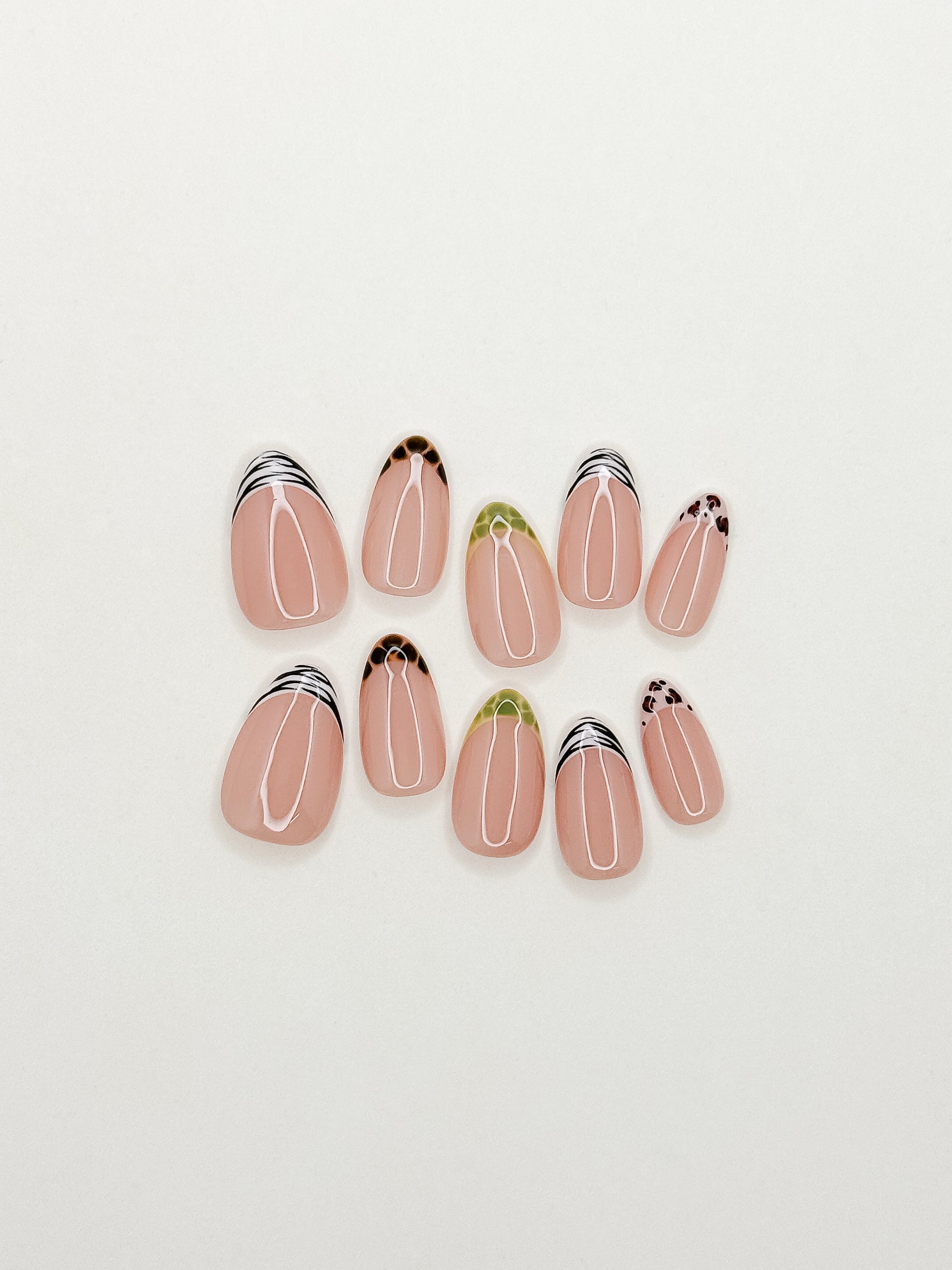 The Wild Card handmade press-on nails arranged on a white background, featuring short almond nails with mixed zebra, tortoiseshell, leopard and green reptile-inspired skinny French tips.
