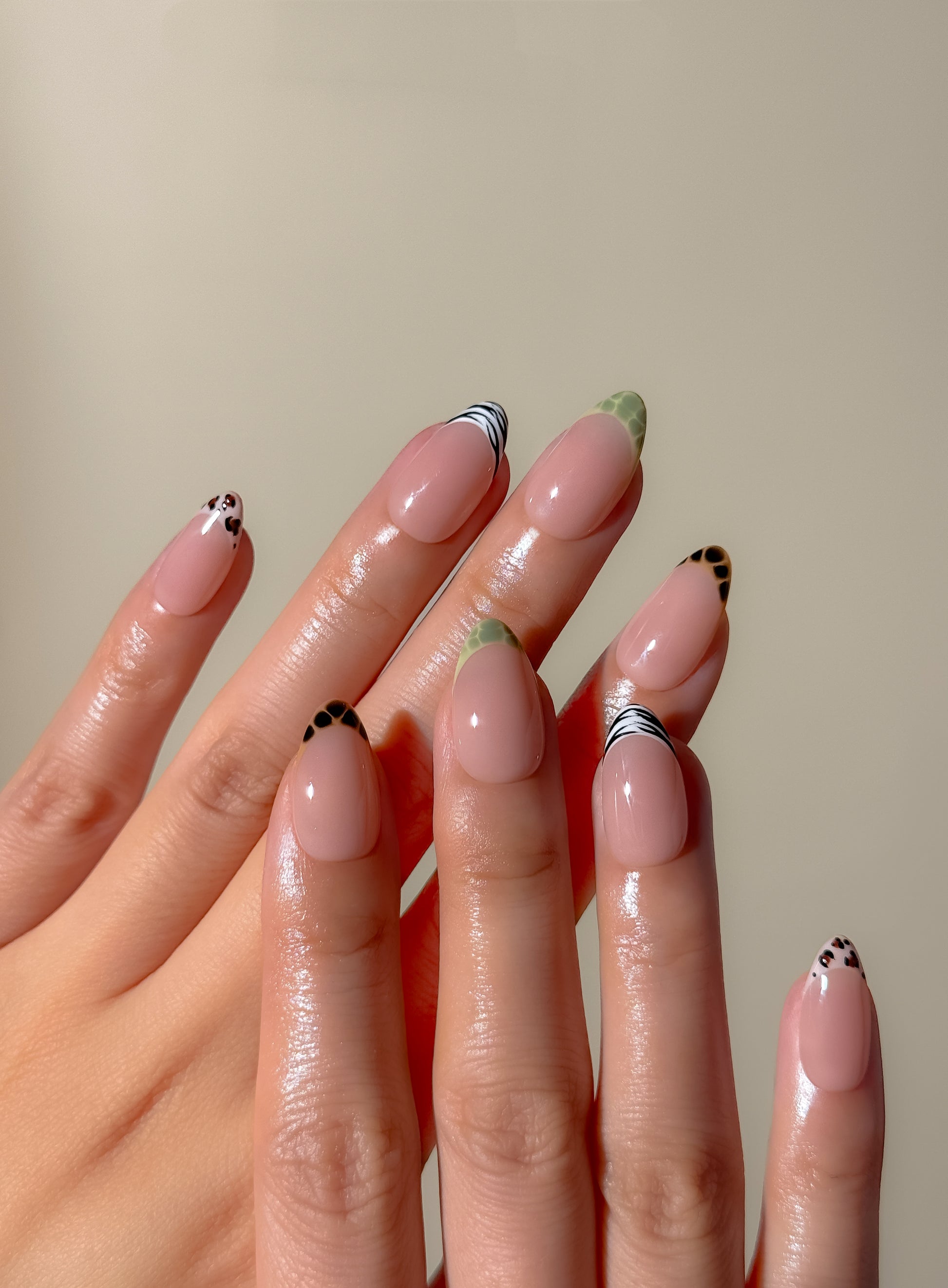 Close-up of The Wild Card handmade press-on nails, featuring zebra stripes, tortoiseshell spots, green reptile-inspired tips and small leopard accents on a short almond shape.